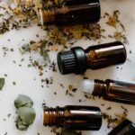 Flat lay of amber glass bottles and dried herbs for aromatherapy on a white surface.